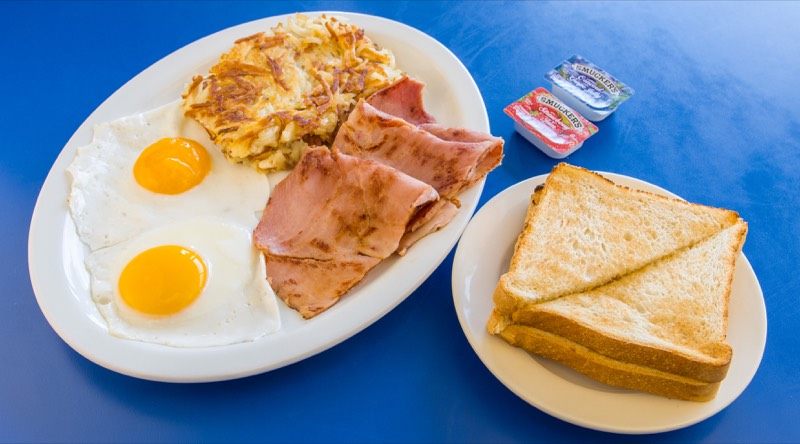 Two eggs over easy with grilled ham, hash browns, and buttered toast.