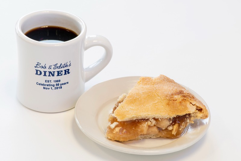 Apple pie slice beside a branded Bob & Edith's coffee mug.