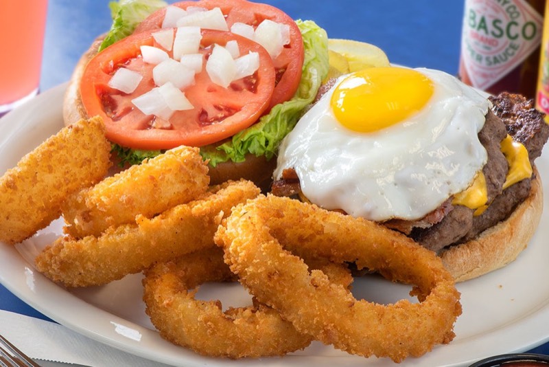 Bacon cheeseburger topped with a sunny-side-up egg beside onion rings.