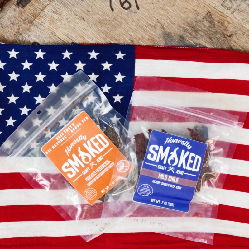 Two Honestly Smoked jerky pouches styled on an American flag over a wood crate.