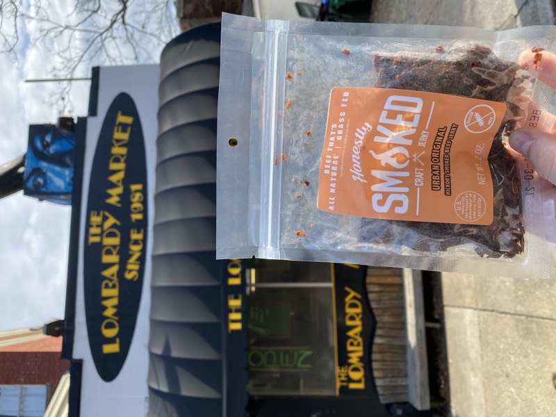 Hand holding an Honestly Smoked jerky bag in front of a market storefront.
