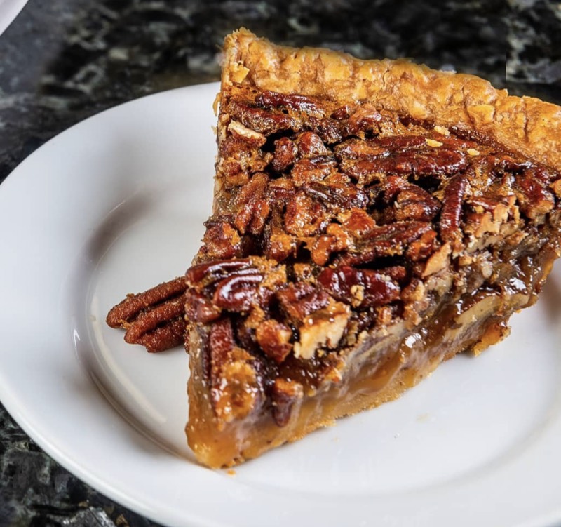 Glossy slice of pecan pie on a white plate over dark marble.