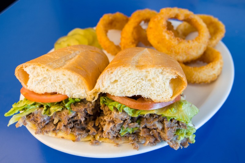 Cheesesteak sub with lettuce and tomato served with a stack of onion rings.