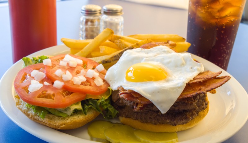 Diner burger with a runny egg and bacon, fries, tomato, and pickles.